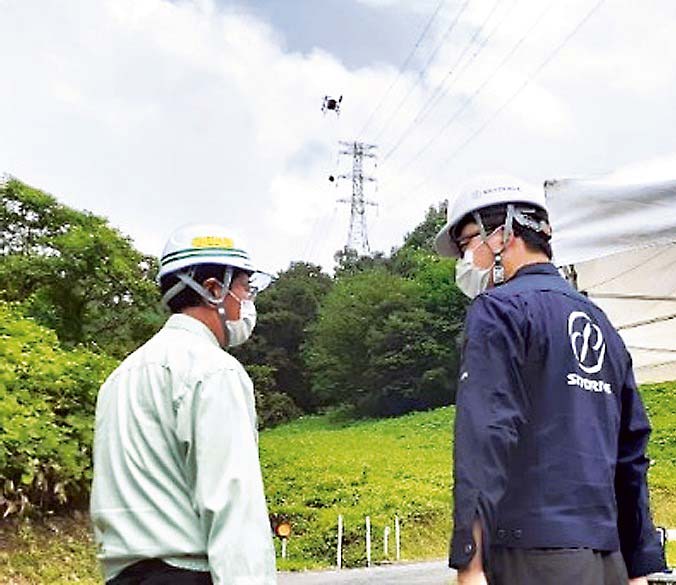 20キログラムの一斗缶を運ぶ様子と、石井浩一中電工業社長（左）、福澤知浩SkyDrive代表取締役CEO