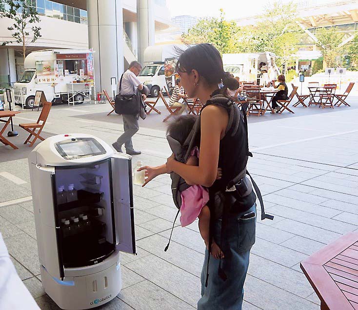 ロボットが改札を通過した親子連れを認識し、ジュースを配布する