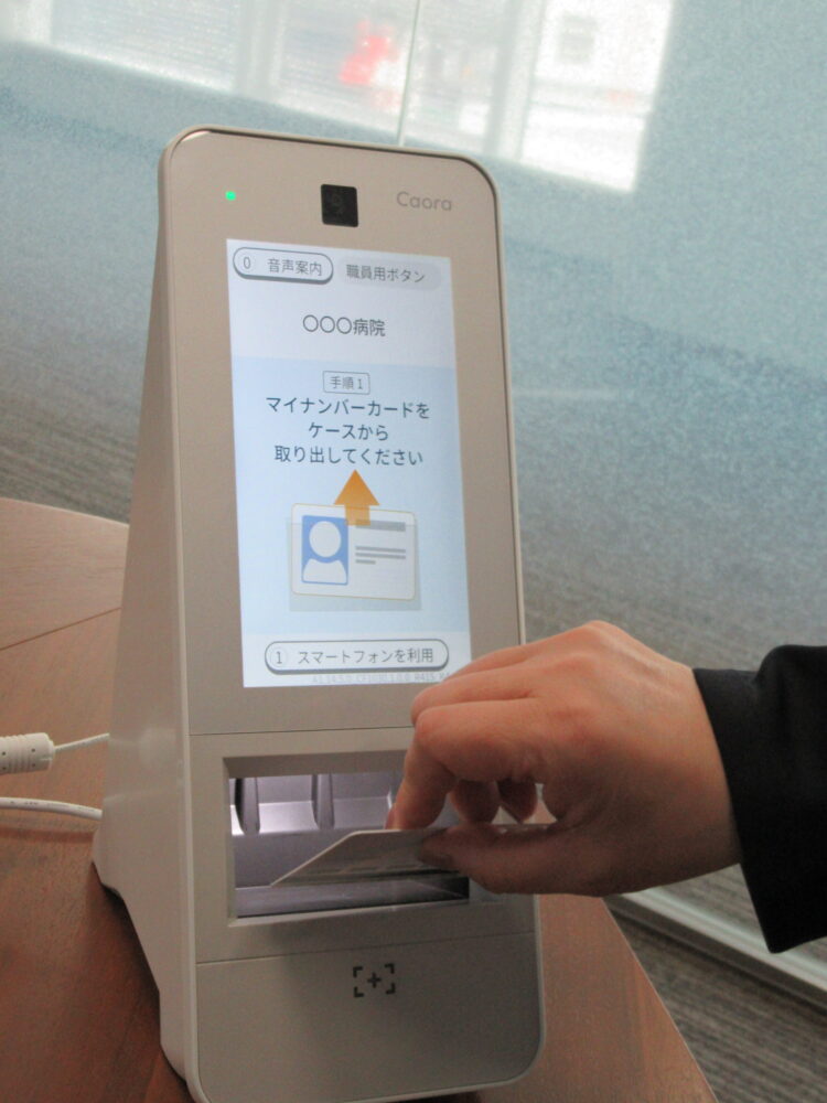 マイナンバーカードを読み取り部へ置く「Caora 2」。画面とカメラ、カード、スマートフォンの操作部を縦一直線に配置した