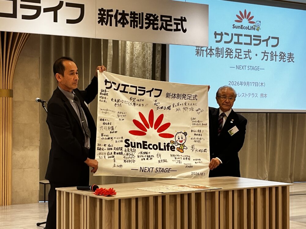 寄せ書きした社旗を披露する太田正昭常務（前でんきや社長、左）と石原政孝社長