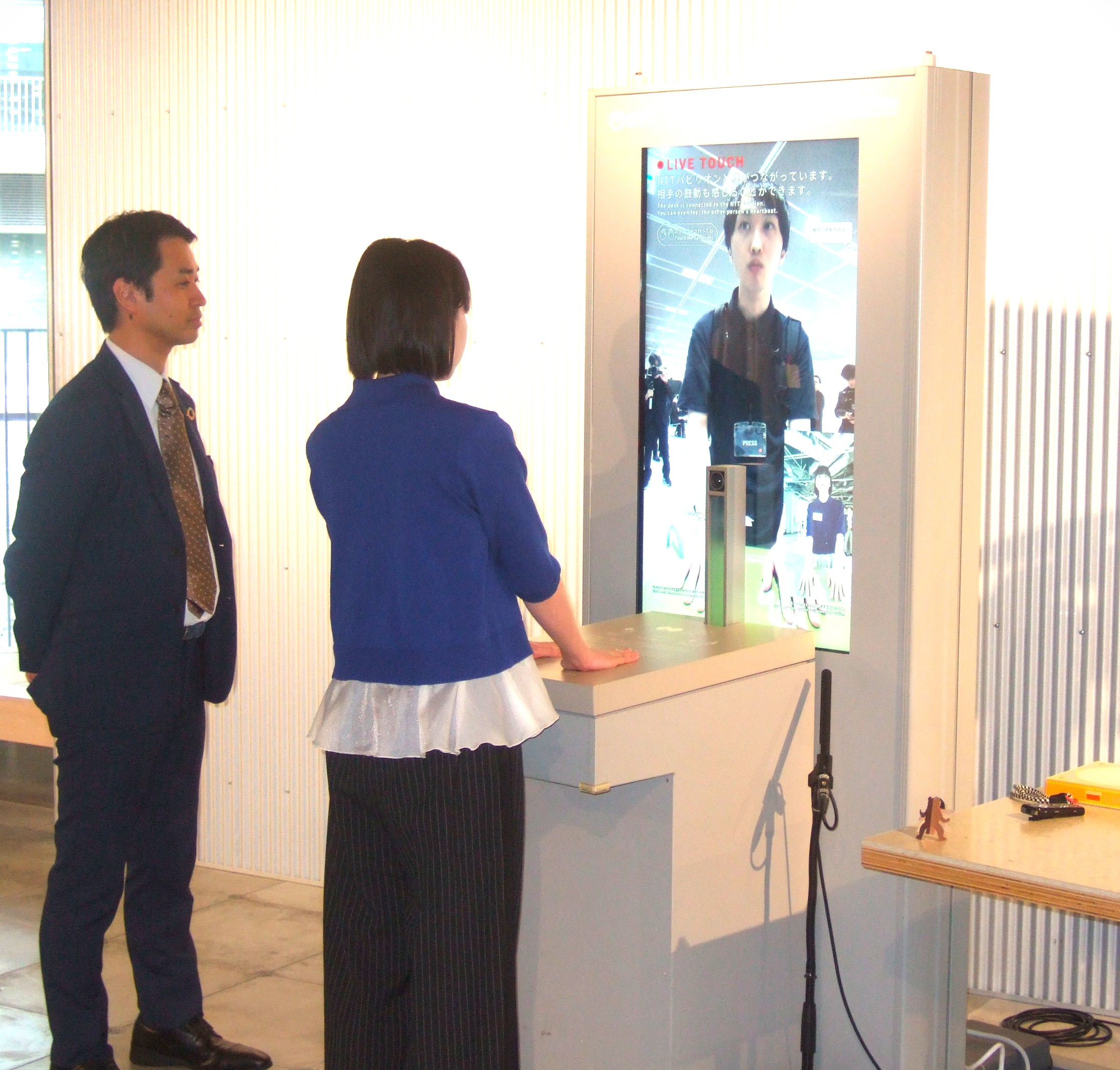 東京会場と結んで行われた「ふれあう伝話」のデモンストレーション。手で板を叩いて振動や胸の鼓動が相手に伝わる